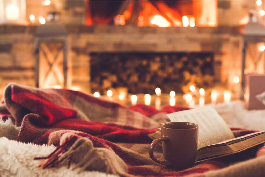 A blanket in front of a roaring fire with a mug and an open book
